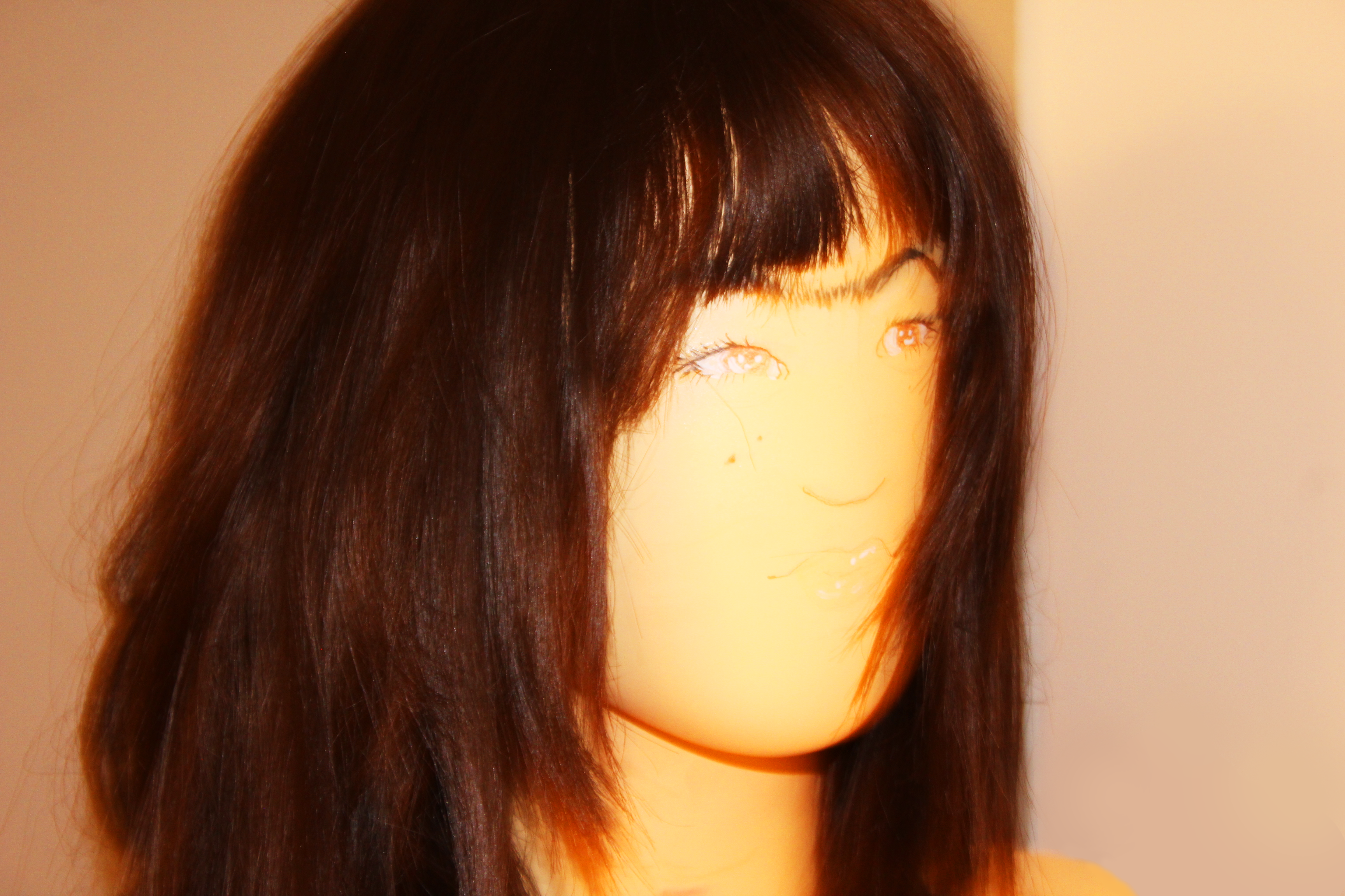 A photo of a young feminine man with long brown hair and a fringe, he has a unibrow and two moles on his cheek as well as one over his left eyebrow, his is photographed in soft light and looks glowing